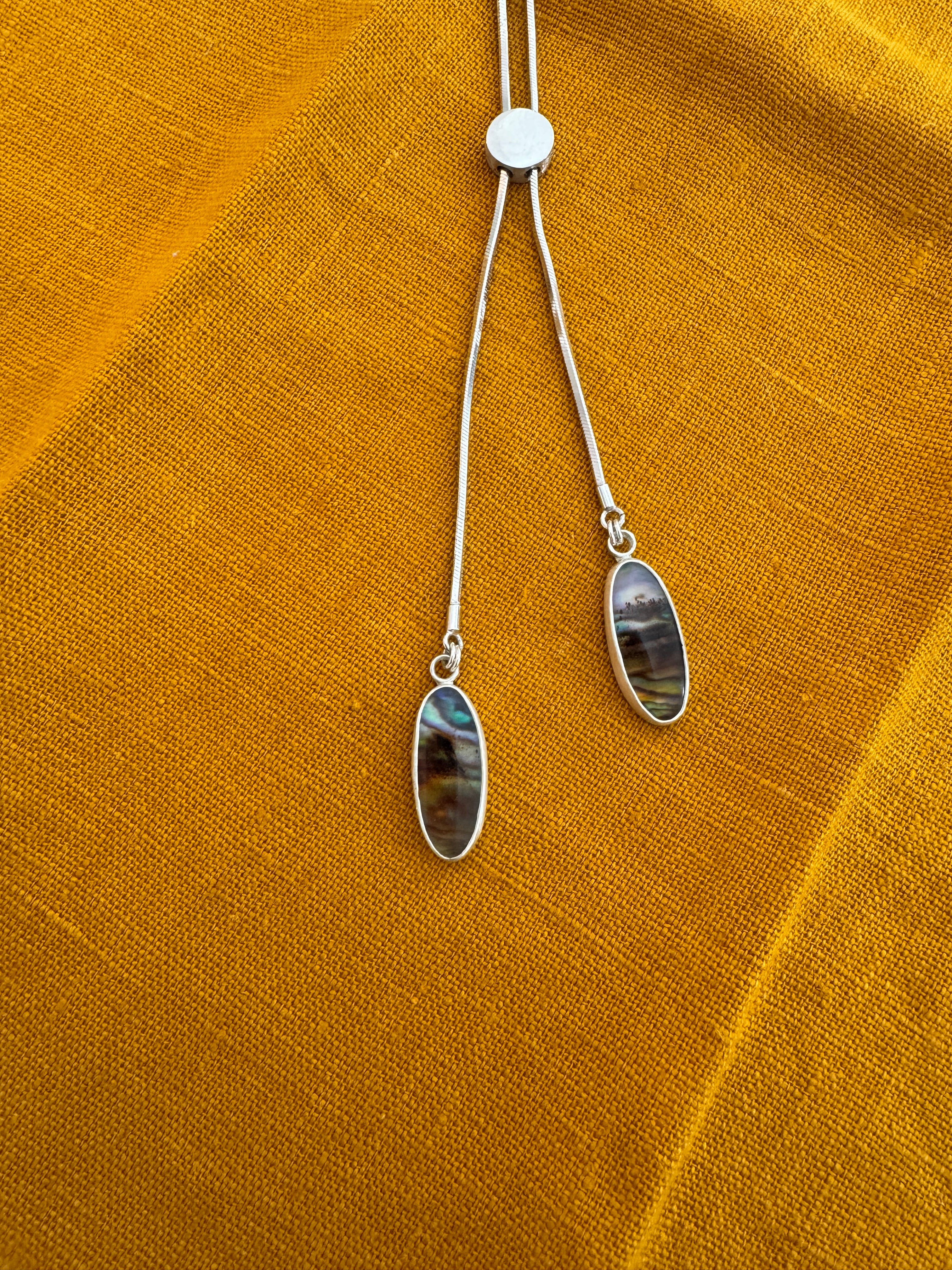 sterling silver bolo style necklace with two pendant stones of Montana agate layered over abalone on a mustard yellow fabric background