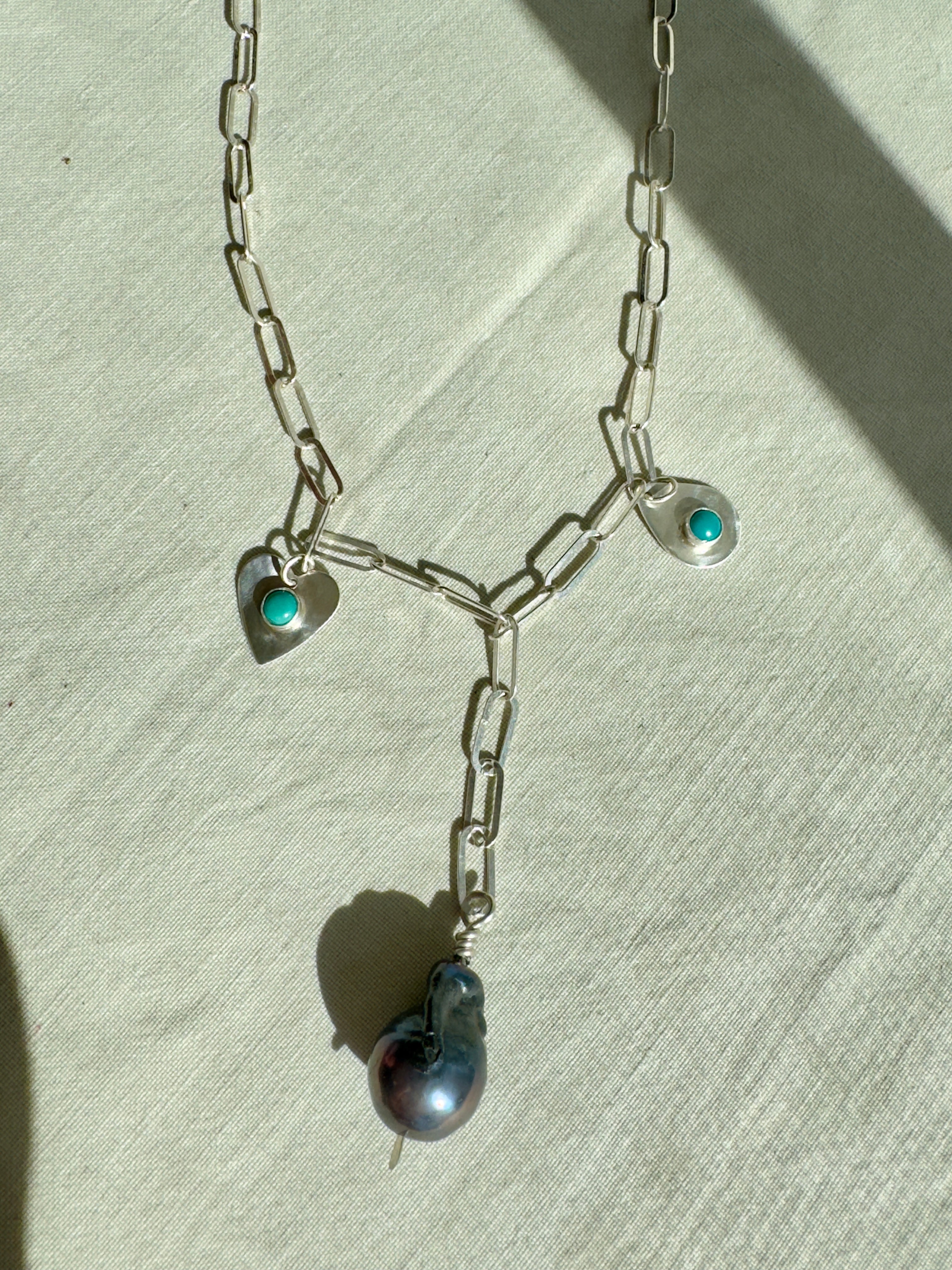 Handmade sterling silver charm necklace with beautiful blue gray baroque pearl in the center, flanked by sterling silver heart and sterling silver teardrop with blue turquoise. This one of a kind charm necklace looks stunning on.
