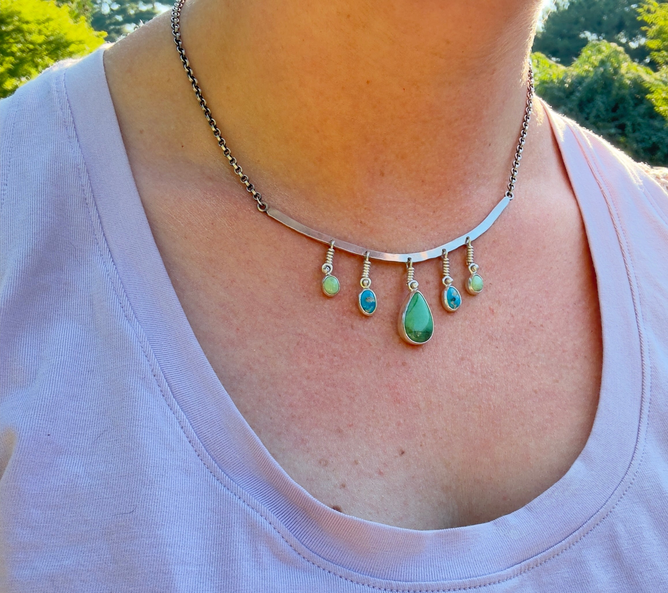 Sterling Silver hammered bar necklace with beautiful green Lucid center stone, flanked by two bright blue castle dome stones and two pale green lucin variscite stones for a total of five stones. The sterling silver bar is attached to a 2.7mm flat rolo chain, oxidized to give it a darker color, with a sterling silver toggle clasp. The necklace rests right on your collarbone, making it the perfect necklace to dress up or down.