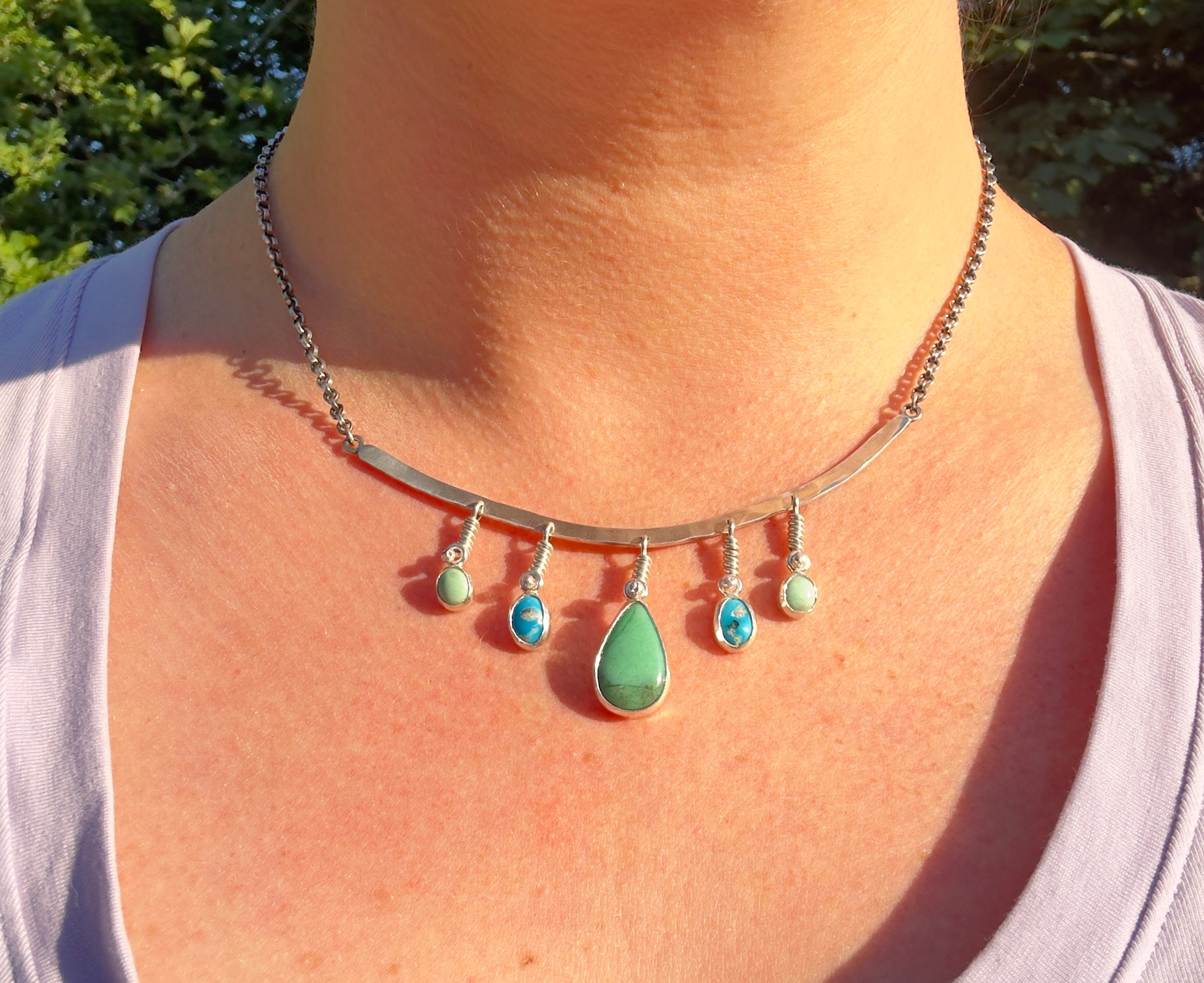 Sterling Silver hammered bar necklace with beautiful green Lucid center stone, flanked by two bright blue castle dome stones and two pale green lucin variscite stones for a total of five stones. The sterling silver bar is attached to a 2.7mm flat rolo chain, oxidized to give it a darker color, with a sterling silver toggle clasp. The necklace rests right on your collarbone, making it the perfect necklace to dress up or down.