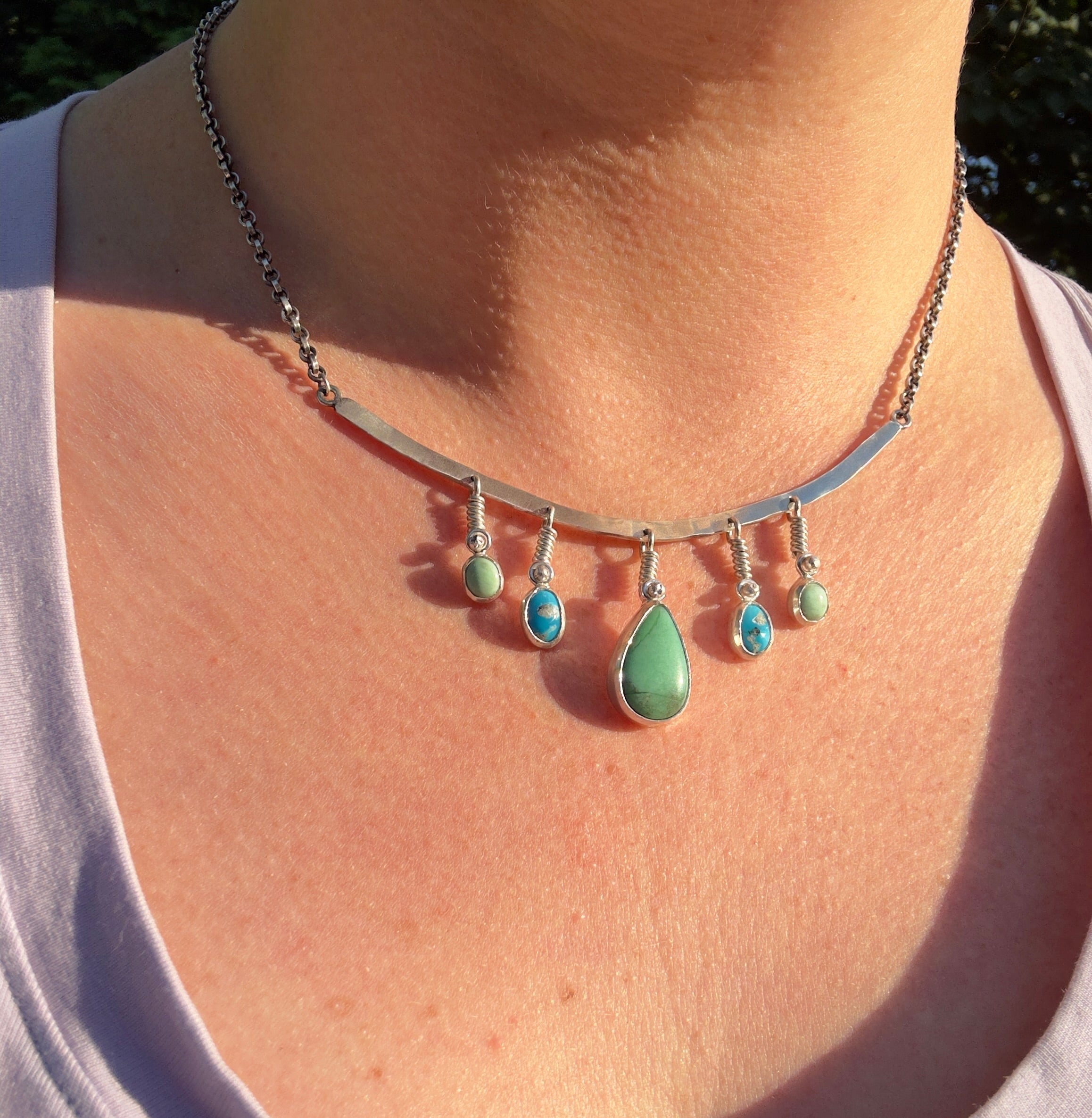 Sterling Silver hammered bar necklace with beautiful green Lucid center stone, flanked by two bright blue castle dome stones and two pale green lucin variscite stones for a total of five stones. The sterling silver bar is attached to a 2.7mm flat rolo chain, oxidized to give it a darker color, with a sterling silver toggle clasp. The necklace rests right on your collarbone, making it the perfect necklace to dress up or down.