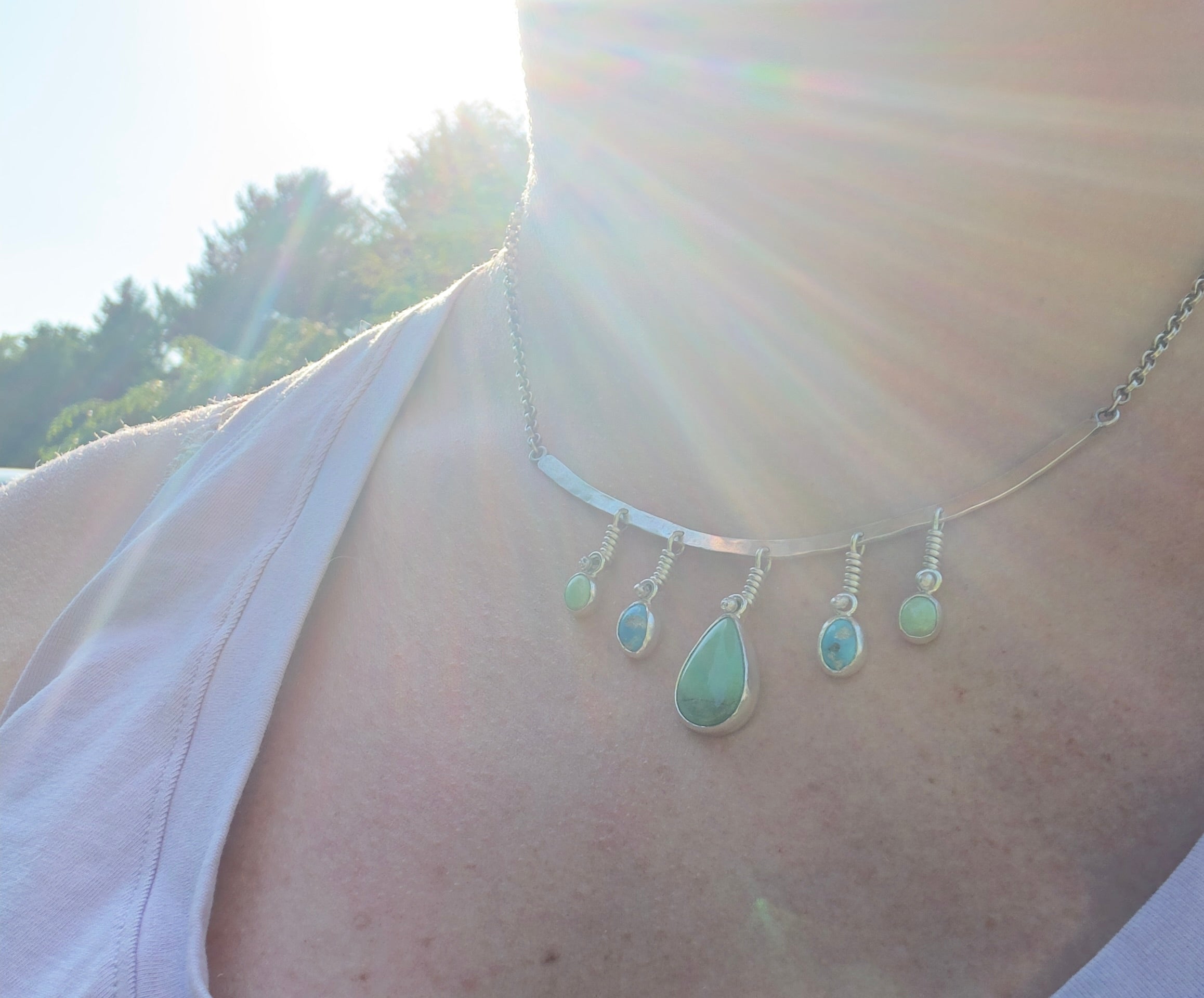 Sterling Silver hammered bar necklace with beautiful green Lucid center stone, flanked by two bright blue castle dome stones and two pale green lucin variscite stones for a total of five stones. The sterling silver bar is attached to a 2.7mm flat rolo chain, oxidized to give it a darker color, with a sterling silver toggle clasp. The necklace rests right on your collarbone, making it the perfect necklace to dress up or down.