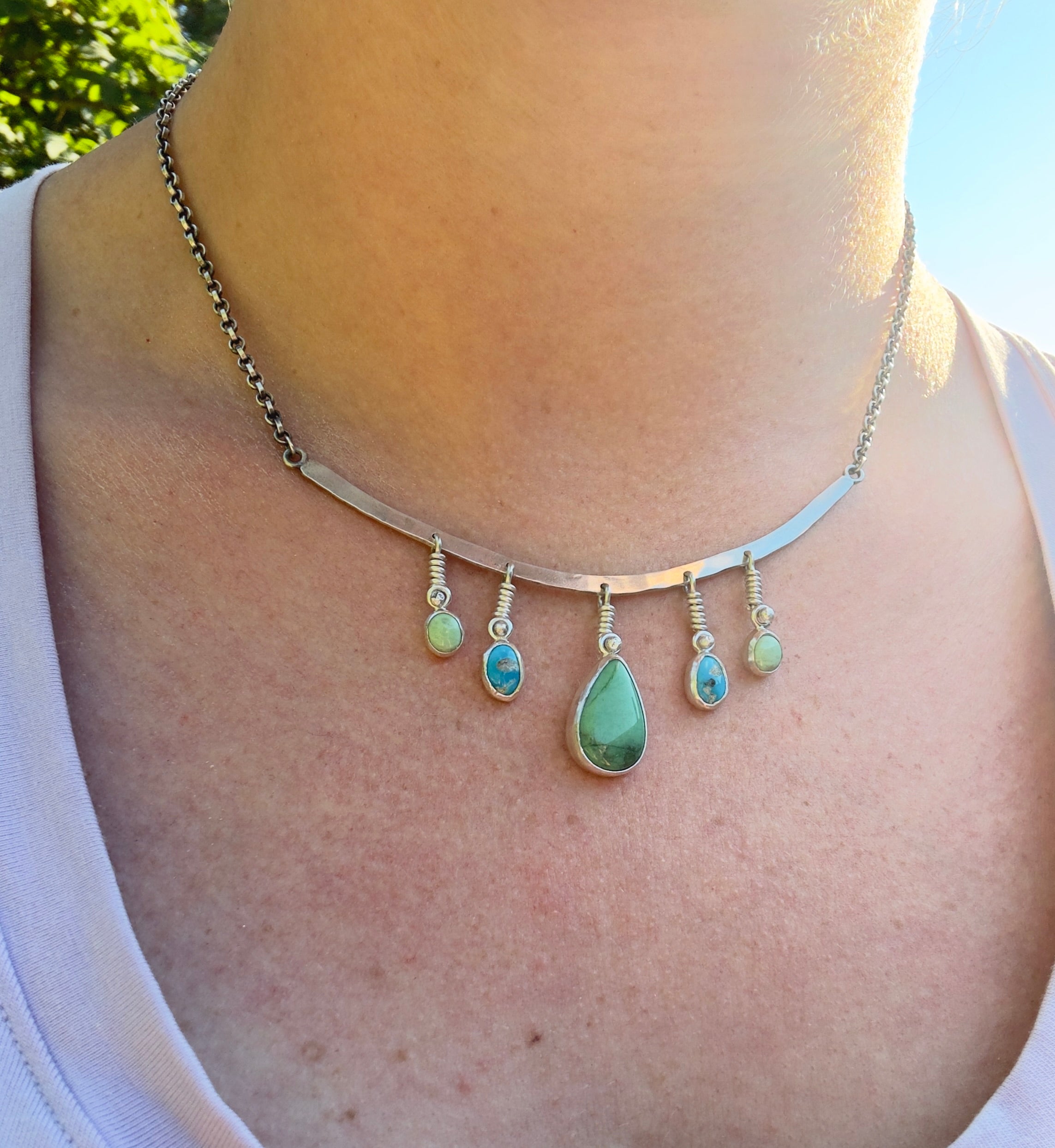 Sterling Silver hammered bar necklace with beautiful green Lucid center stone, flanked by two bright blue castle dome stones and two pale green lucin variscite stones for a total of five stones. The sterling silver bar is attached to a 2.7mm flat rolo chain, oxidized to give it a darker color, with a sterling silver toggle clasp. The necklace rests right on your collarbone, making it the perfect necklace to dress up or down.