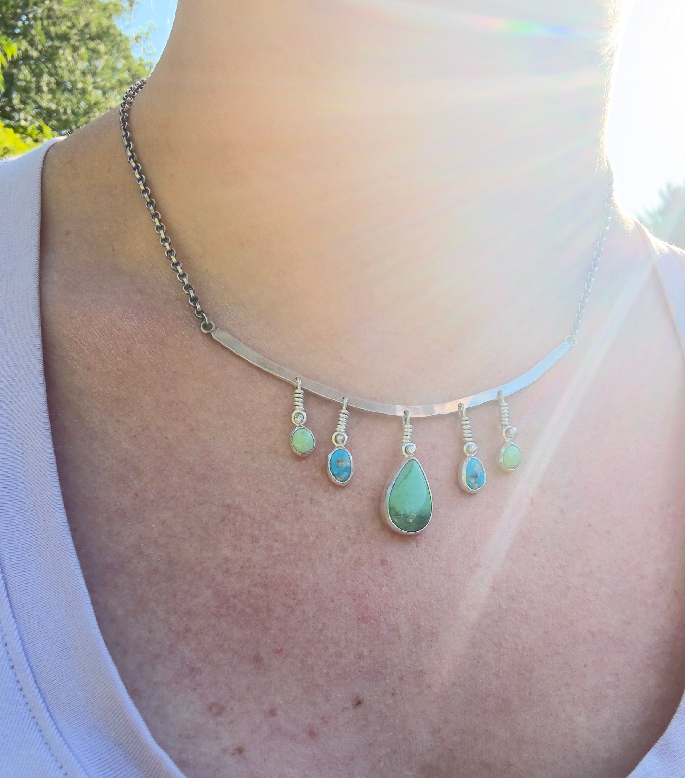 Sterling Silver hammered bar necklace with beautiful green Lucid center stone, flanked by two bright blue castle dome stones and two pale green lucin variscite stones for a total of five stones. The sterling silver bar is attached to a 2.7mm flat rolo chain, oxidized to give it a darker color, with a sterling silver toggle clasp. The necklace rests right on your collarbone, making it the perfect necklace to dress up or down.