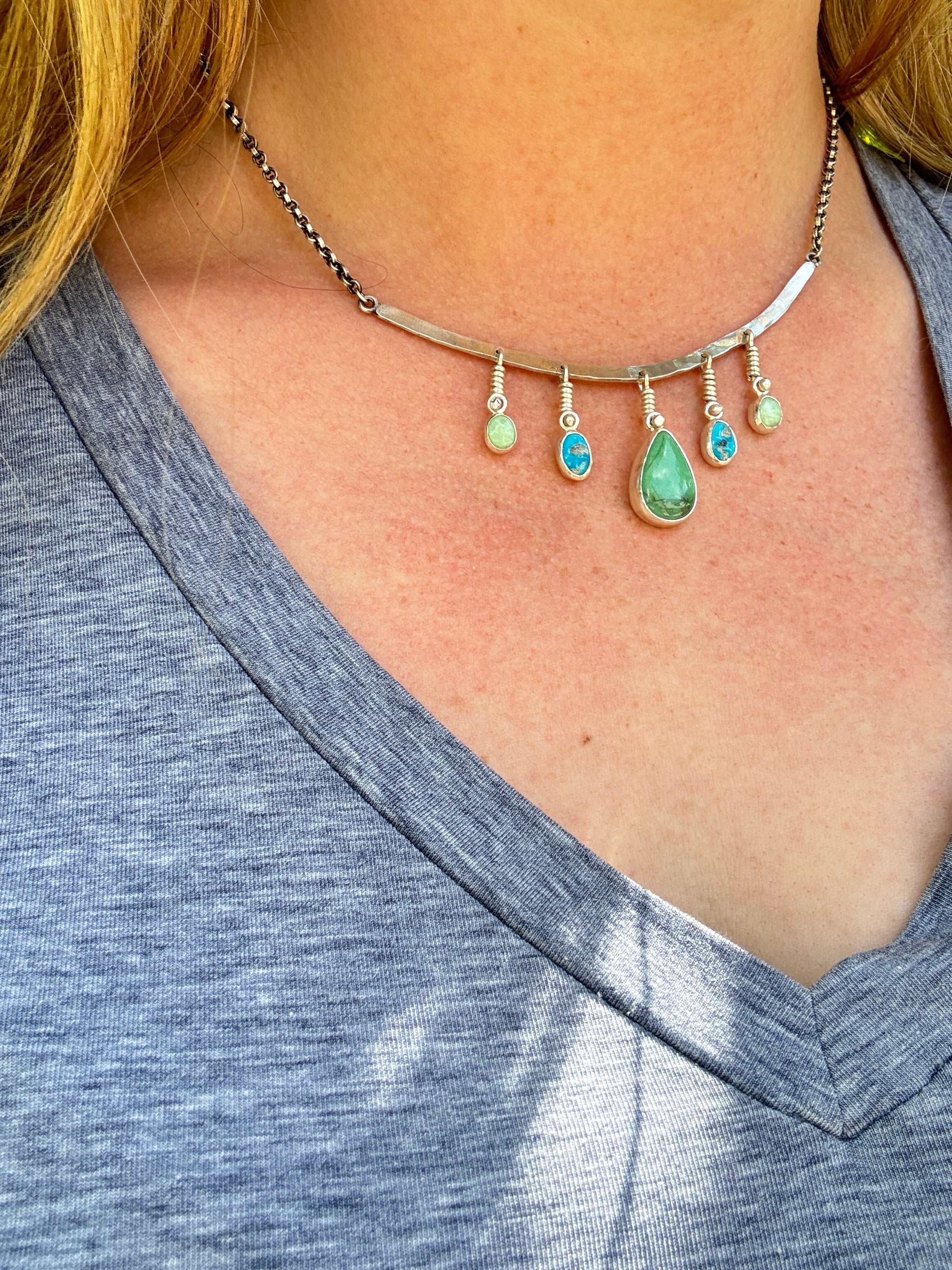 Sterling Silver hammered bar necklace with beautiful green Lucid center stone, flanked by two bright blue castle dome stones and two pale green lucin variscite stones for a total of five stones. The sterling silver bar is attached to a 2.7mm flat rolo chain, oxidized to give it a darker color, with a sterling silver toggle clasp. The necklace rests right on your collarbone, making it the perfect necklace to dress up or down.