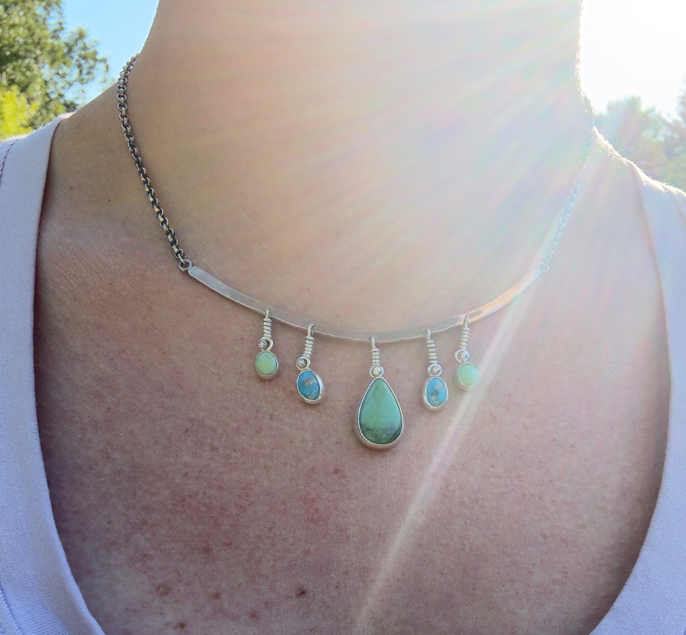 Sterling Silver hammered bar necklace with beautiful green Lucid center stone, flanked by two bright blue castle dome stones and two pale green lucin variscite stones for a total of five stones. The sterling silver bar is attached to a 2.7mm flat rolo chain, oxidized to give it a darker color, with a sterling silver toggle clasp. The necklace rests right on your collarbone, making it the perfect necklace to dress up or down.