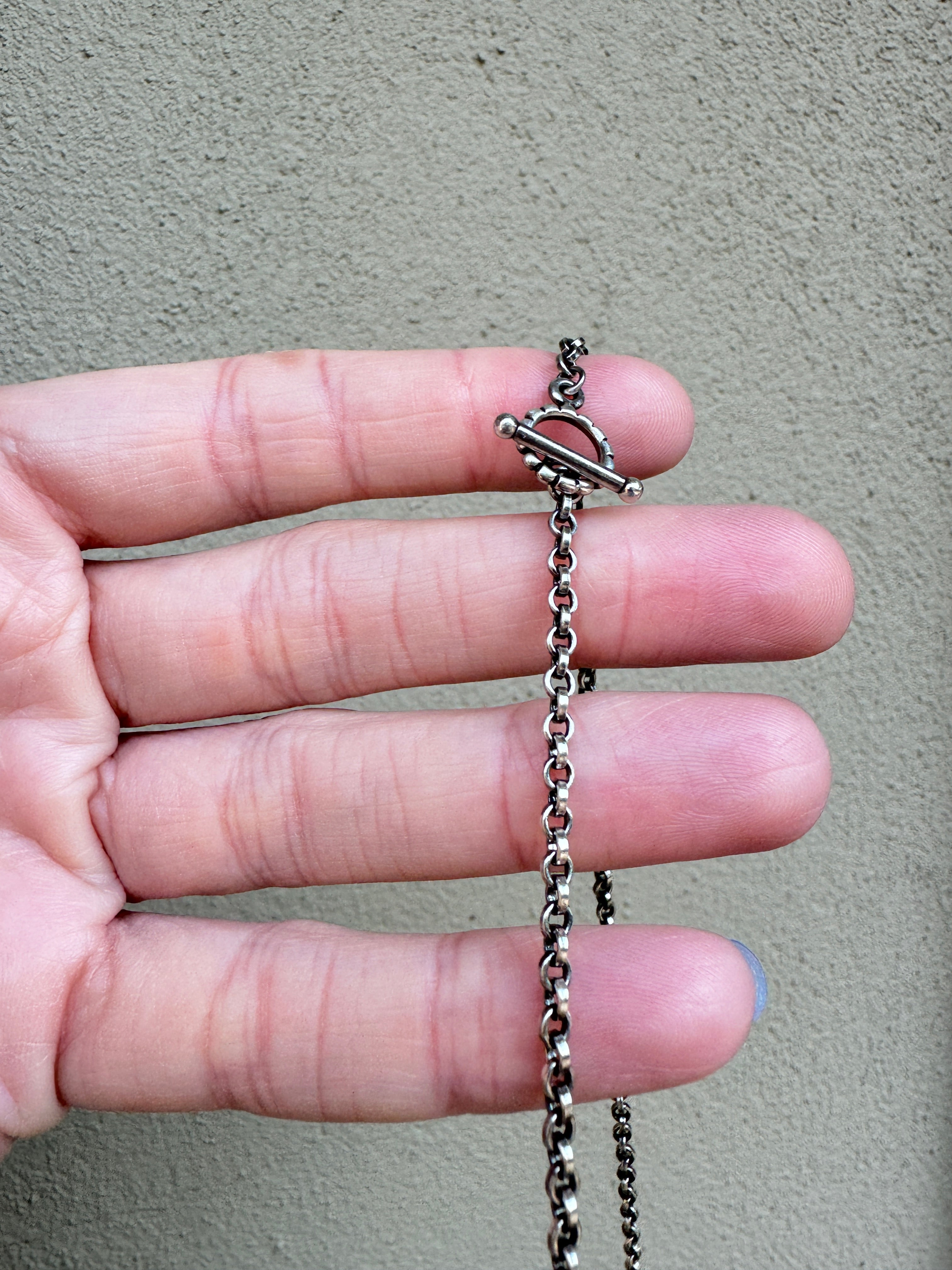Sterling Silver hammered bar necklace with beautiful green Lucid center stone, flanked by two bright blue castle dome stones and two pale green lucin variscite stones for a total of five stones. The sterling silver bar is attached to a 2.7mm flat rolo chain, oxidized to give it a darker color, with a sterling silver toggle clasp. The necklace rests right on your collarbone, making it the perfect necklace to dress up or down.