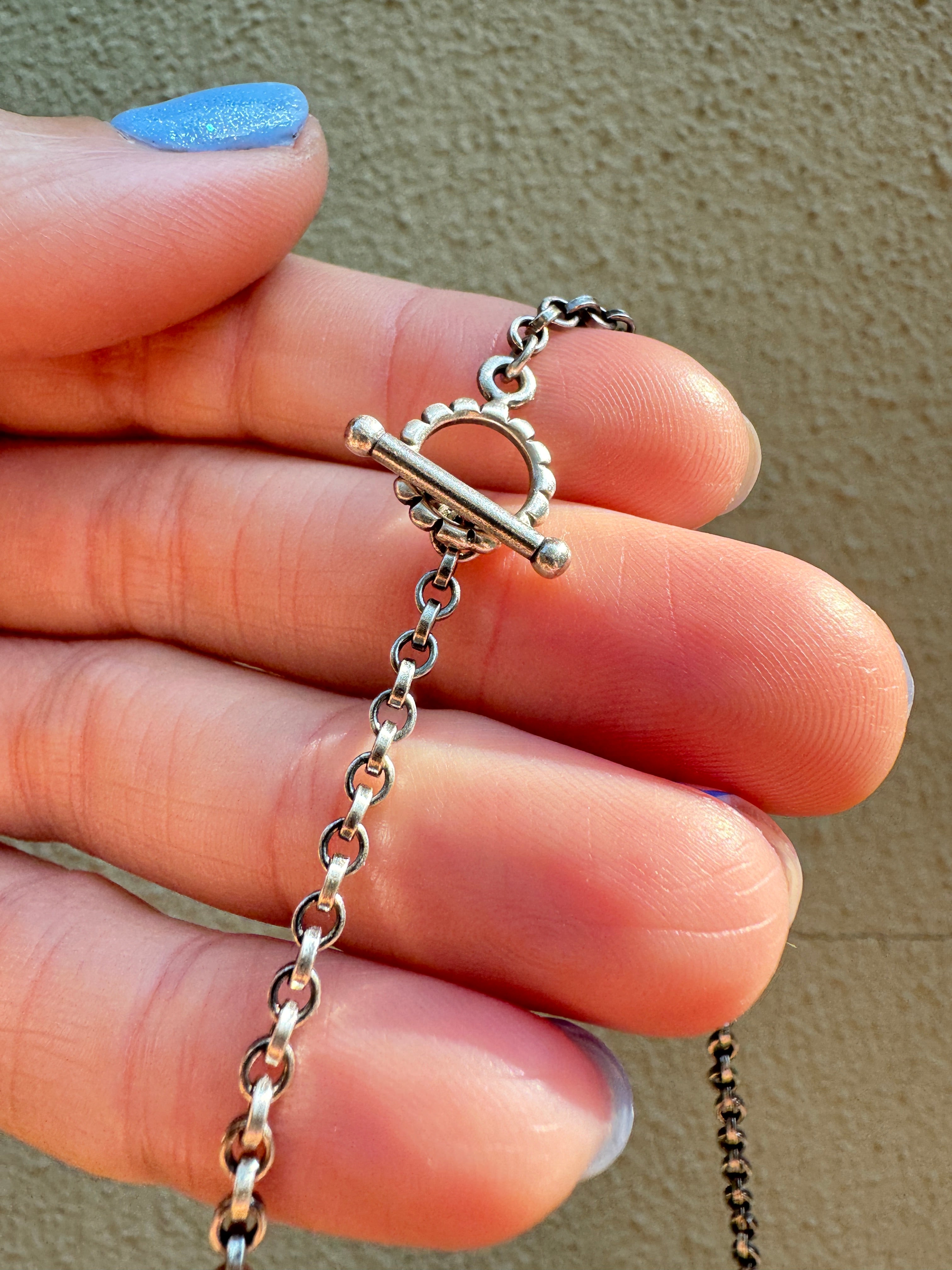Sterling Silver hammered bar necklace with beautiful green Lucid center stone, flanked by two bright blue castle dome stones and two pale green lucin variscite stones for a total of five stones. The sterling silver bar is attached to a 2.7mm flat rolo chain, oxidized to give it a darker color, with a sterling silver toggle clasp. The necklace rests right on your collarbone, making it the perfect necklace to dress up or down.