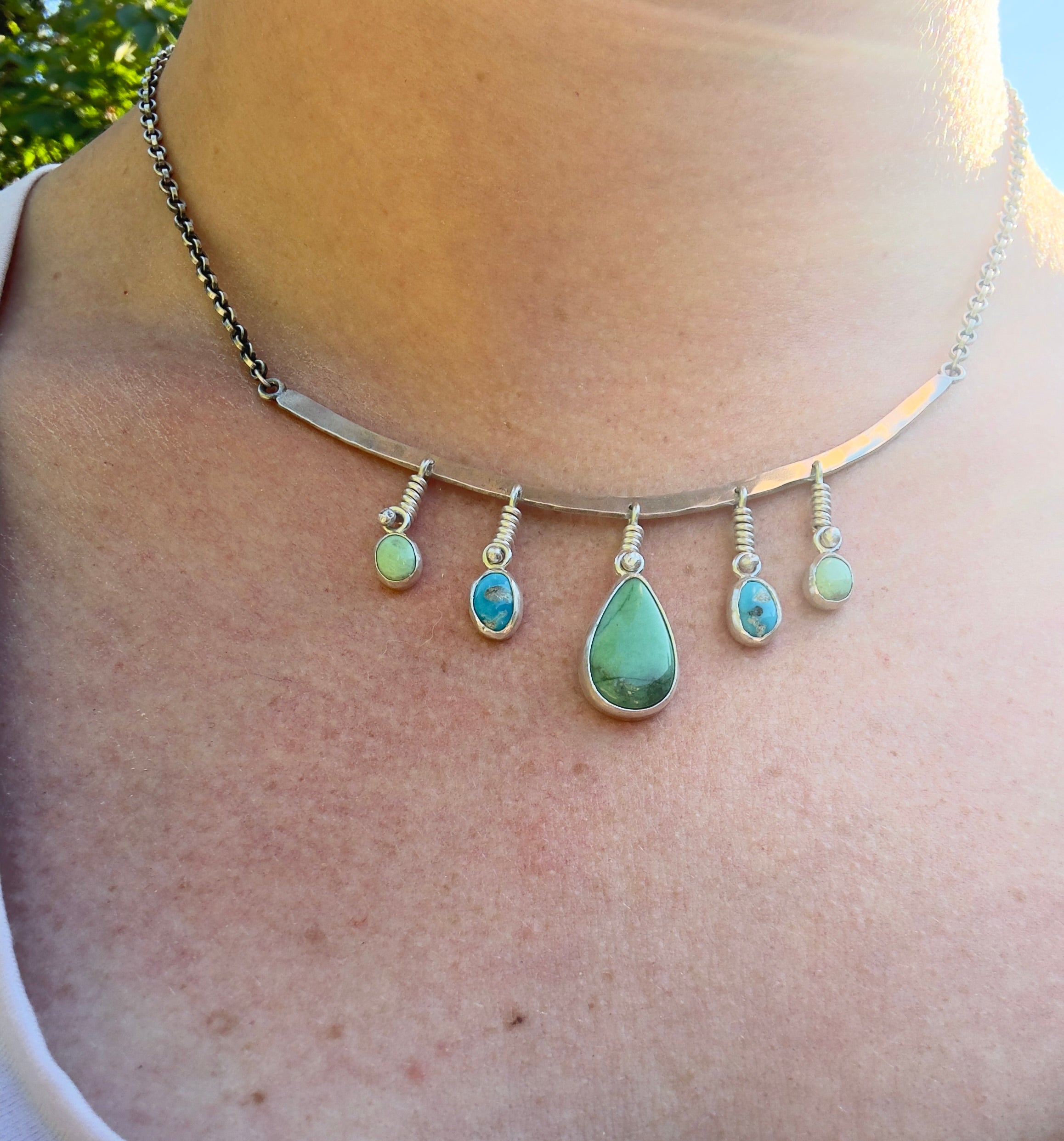 Sterling Silver hammered bar necklace with beautiful green Lucid center stone, flanked by two bright blue castle dome stones and two pale green lucin variscite stones for a total of five stones. The sterling silver bar is attached to a 2.7mm flat rolo chain, oxidized to give it a darker color, with a sterling silver toggle clasp. The necklace rests right on your collarbone, making it the perfect necklace to dress up or down.