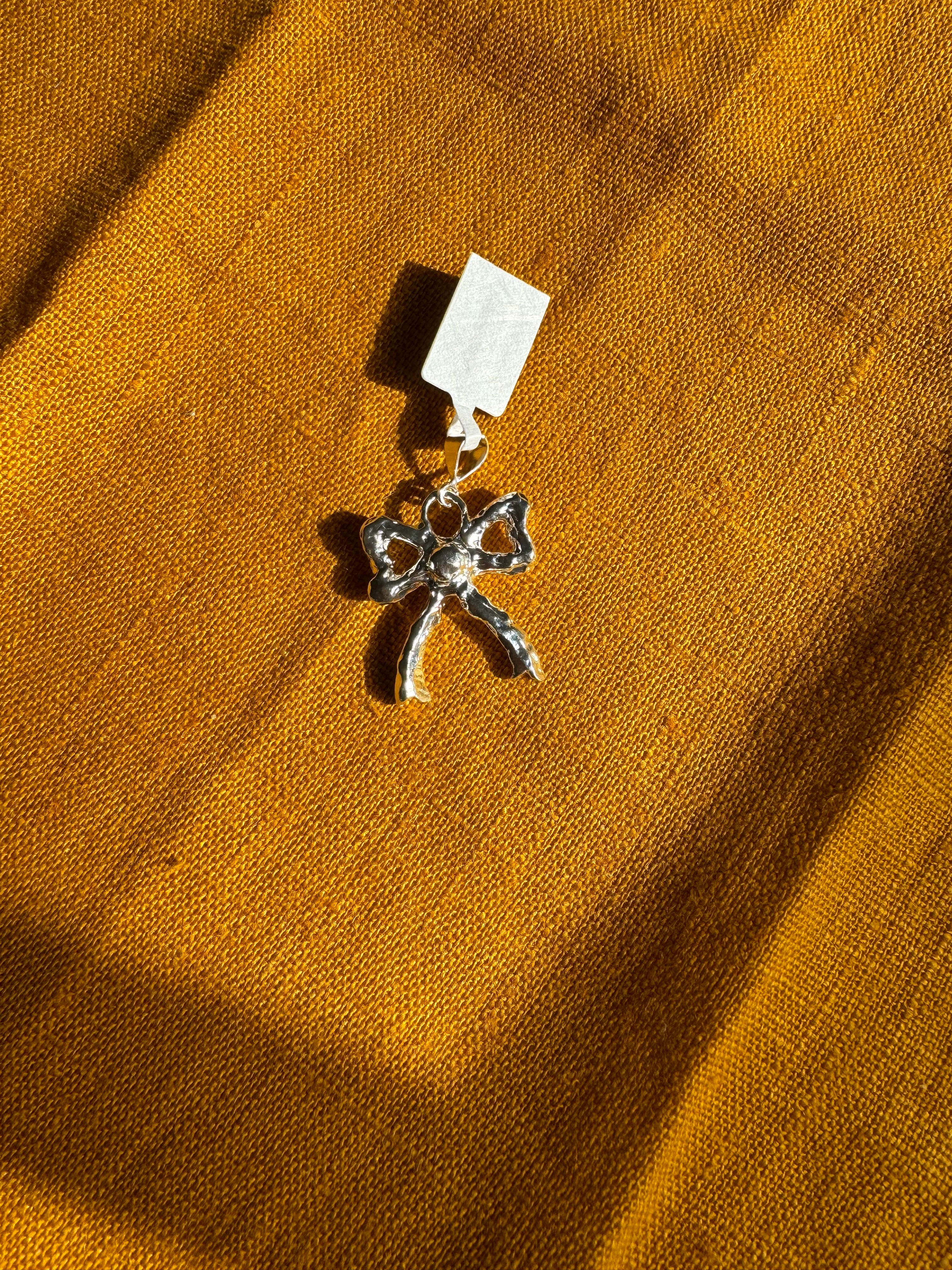 sterling silver bow charm with a tag on a mustard yellow fabric background