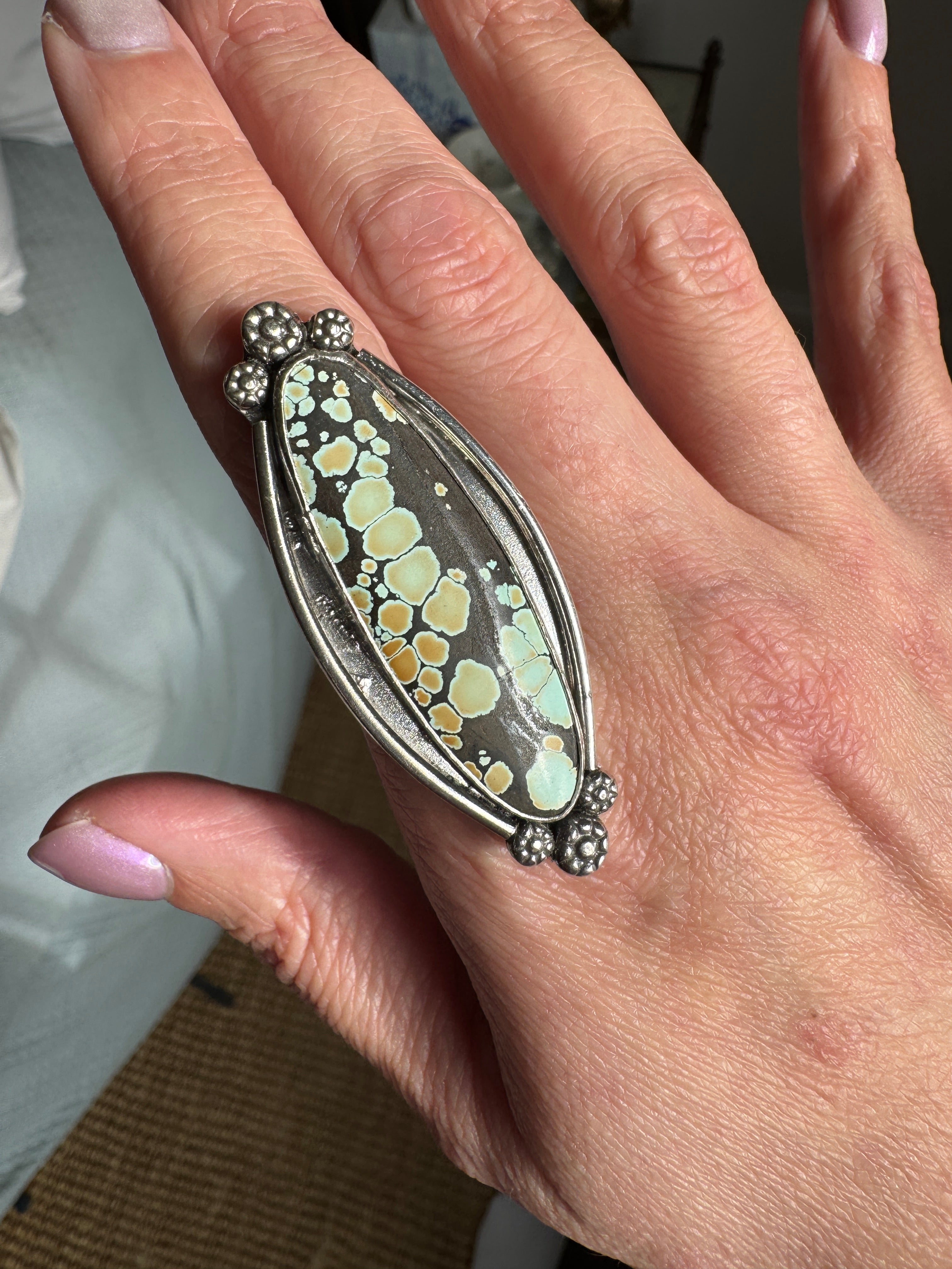 Hand wearing a decorative ring with a green and silver design.