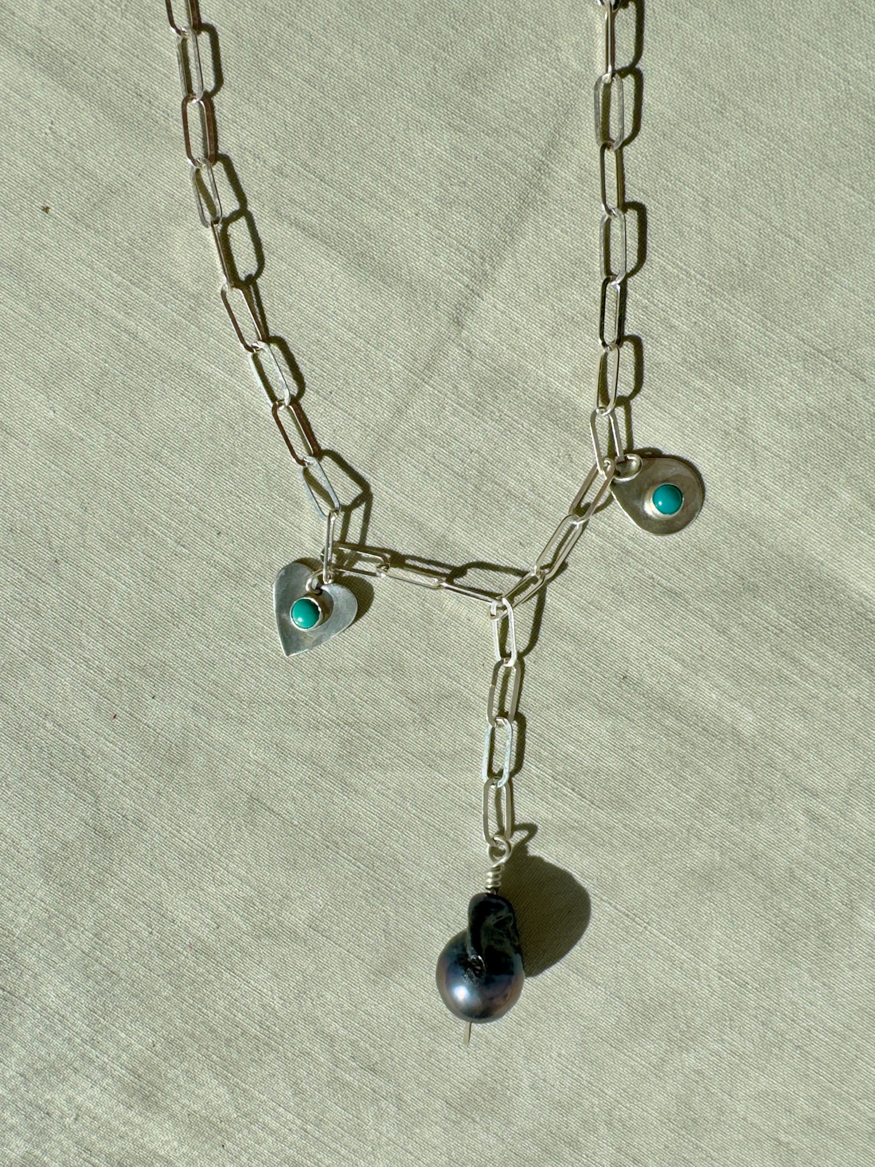 Handmade sterling silver charm necklace with beautiful blue gray baroque pearl in the center, flanked by sterling silver heart and sterling silver teardrop with blue turquoise. This one of a kind charm necklace looks stunning on.