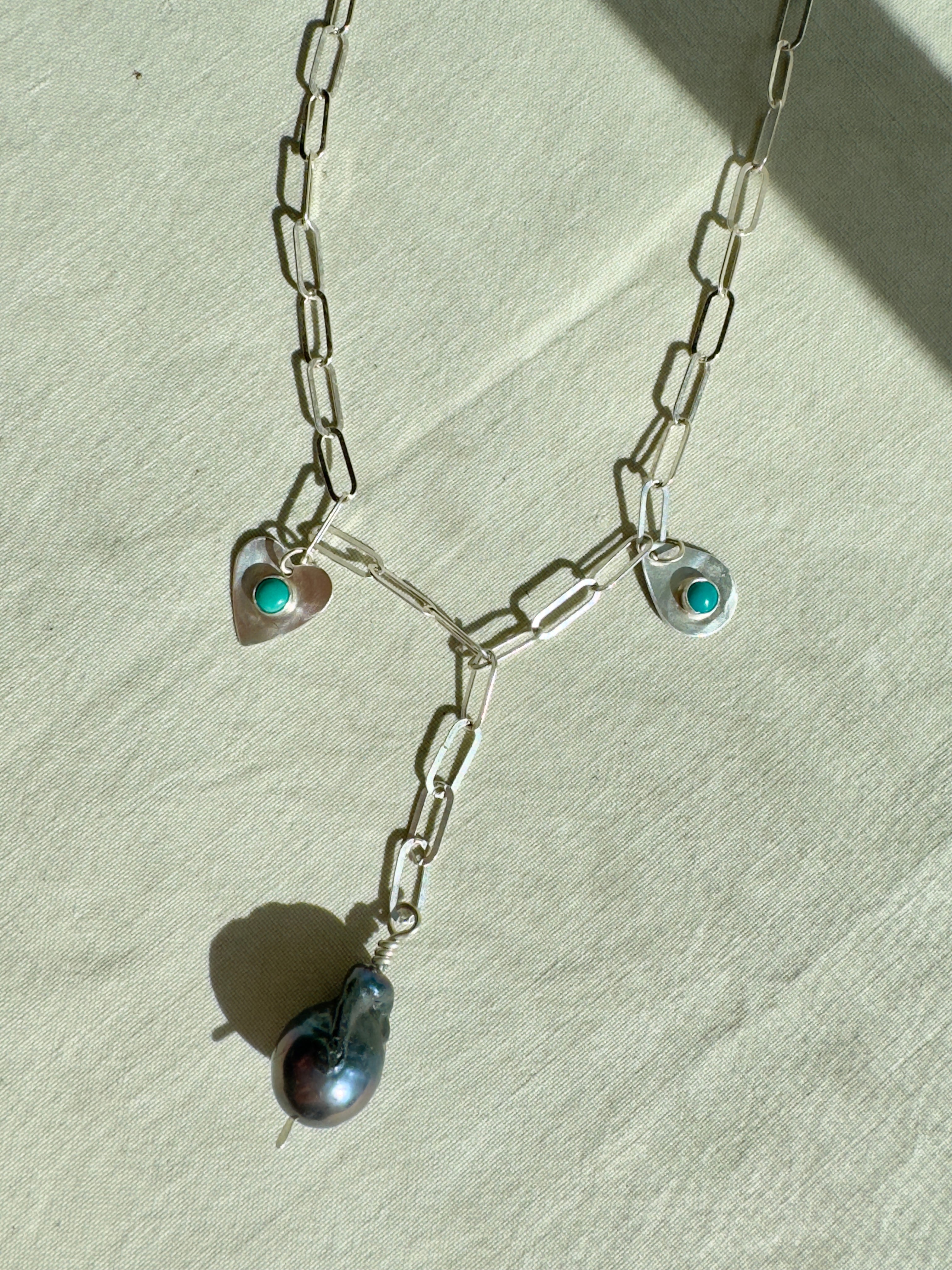Handmade sterling silver charm necklace with beautiful blue gray baroque pearl in the center, flanked by sterling silver heart and sterling silver teardrop with blue turquoise. This one of a kind charm necklace looks stunning on.
