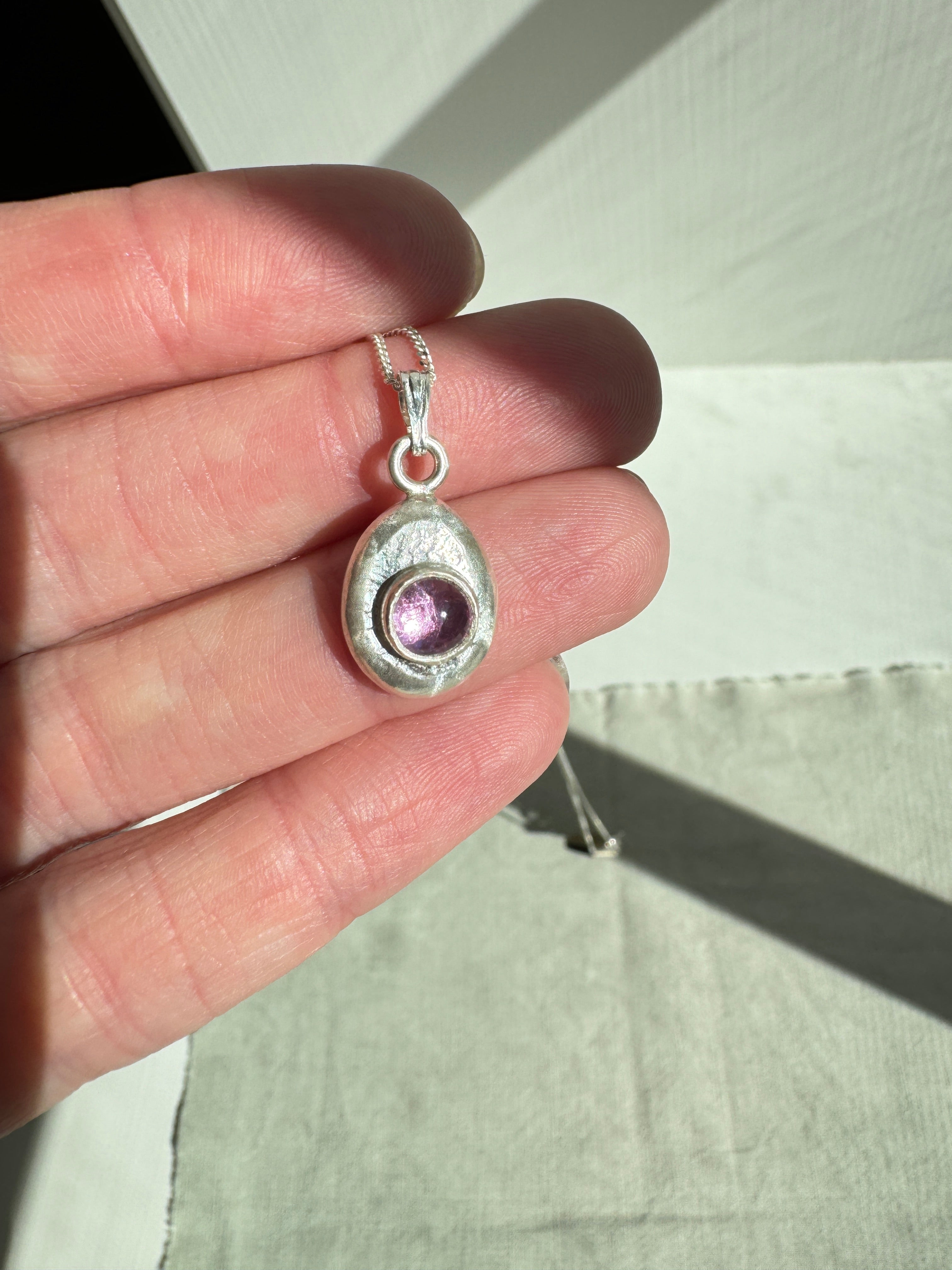6mm Pink Sapphire (lab created) on a hand forged nugget of sterling silver. Choose between a 16” or 18” sterling silver diamond cut curb chain.