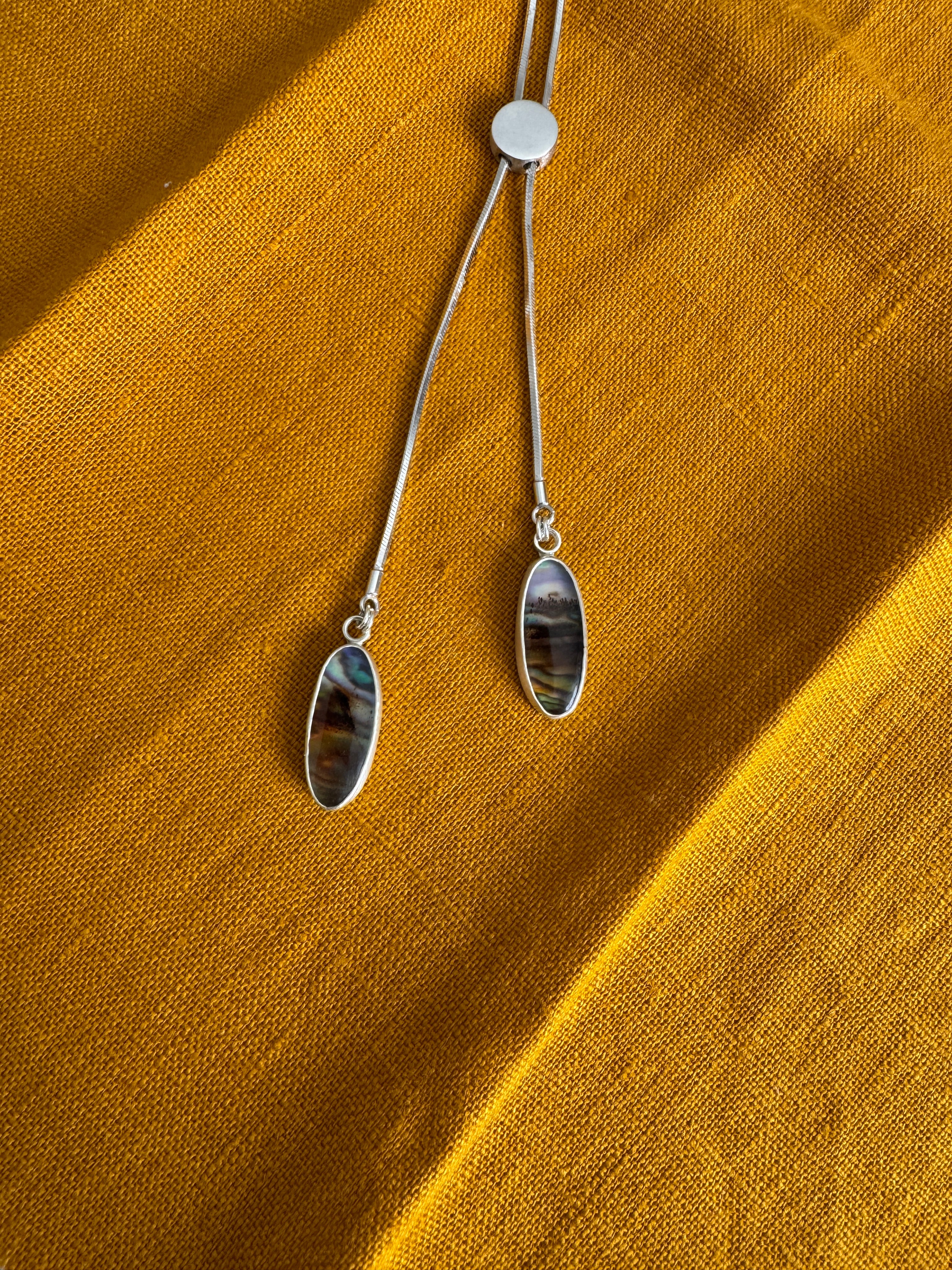 sterling silver bolo style necklace with two pendant stones of Montana agate layered over abalone on a mustard yellow fabric background