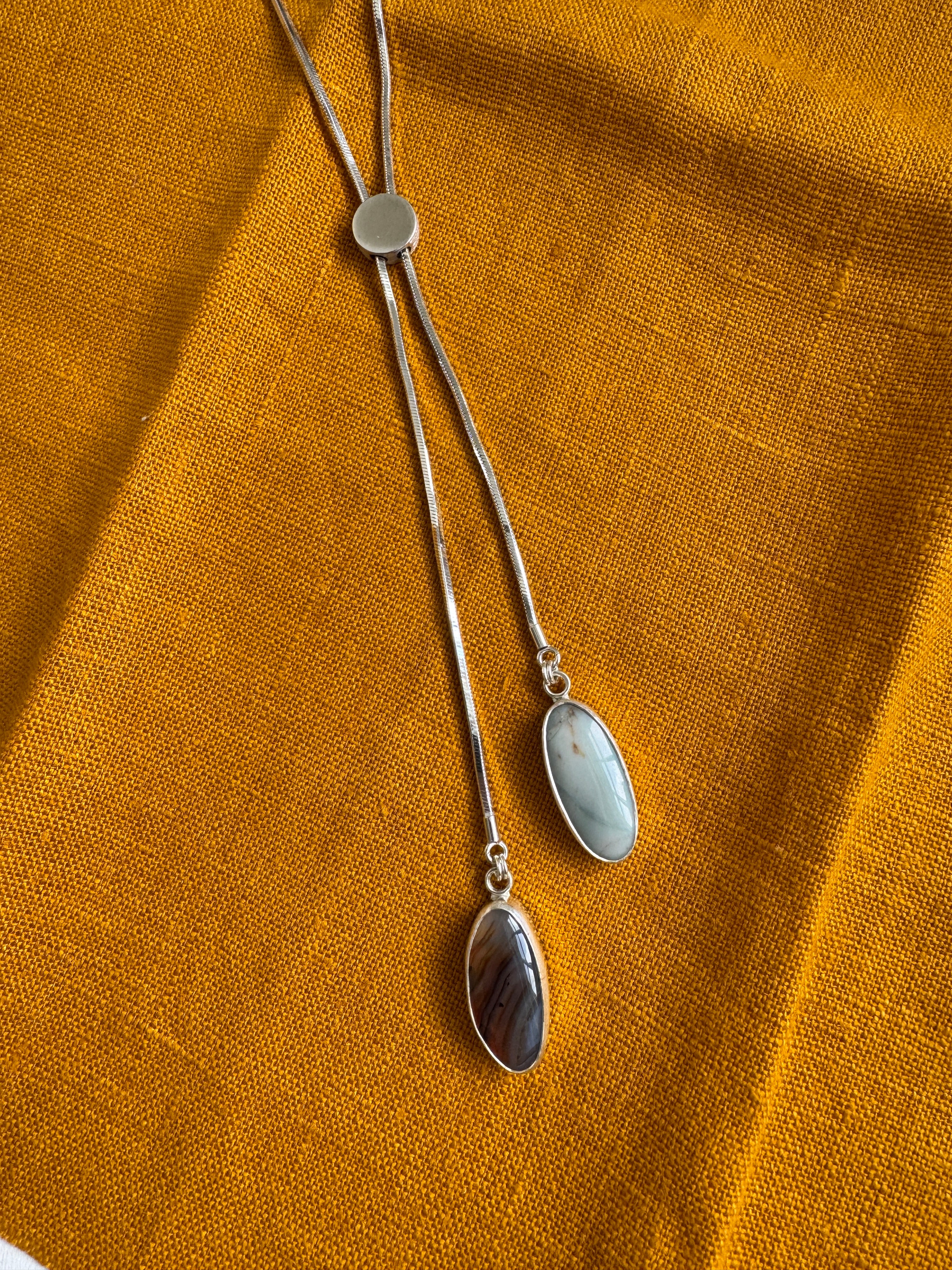 Silver necklace with two pendant stones on a mustard yellow fabric background