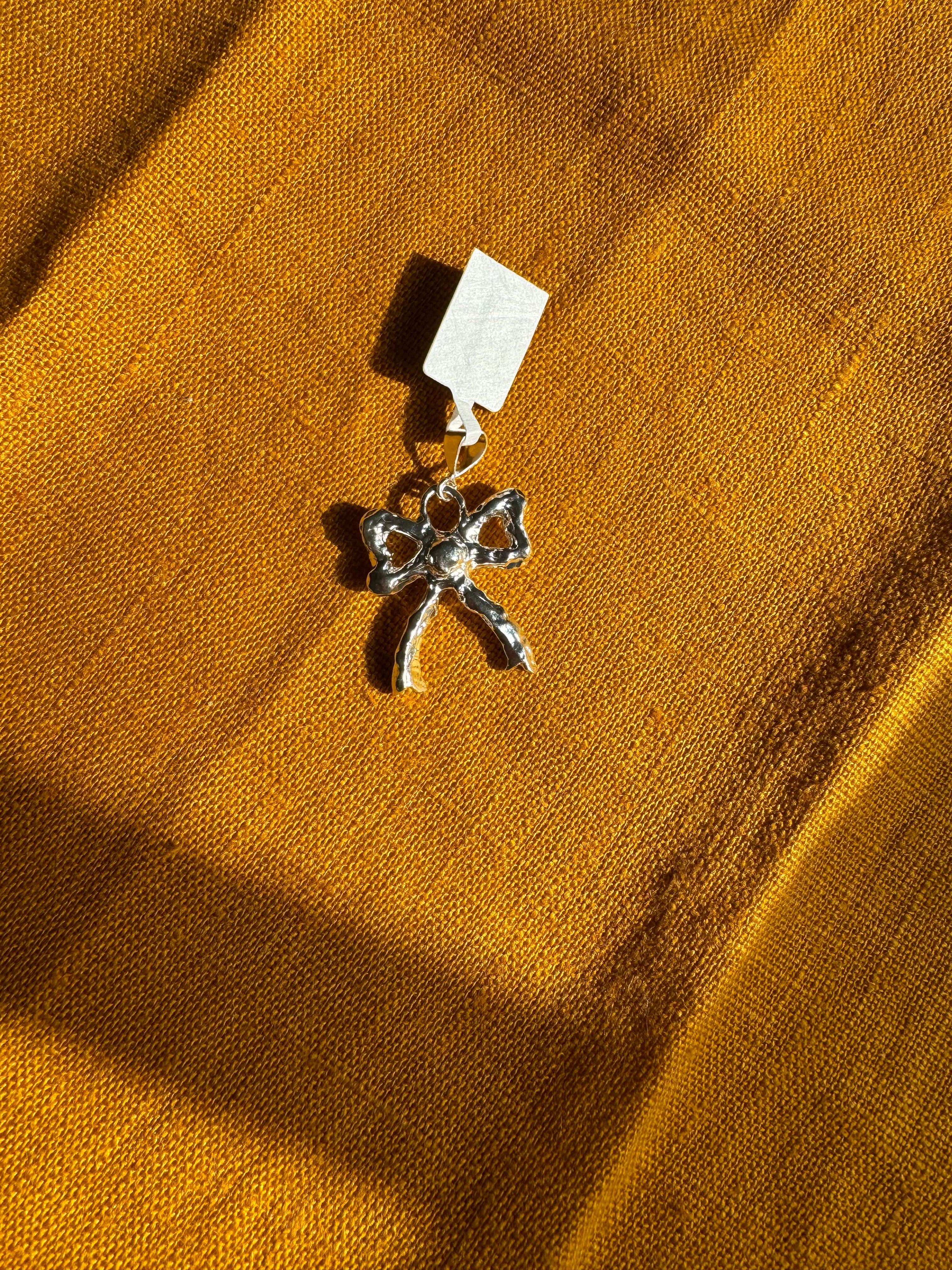 Sterling Silver Bow charm with a tag on a mustard yellow fabric background