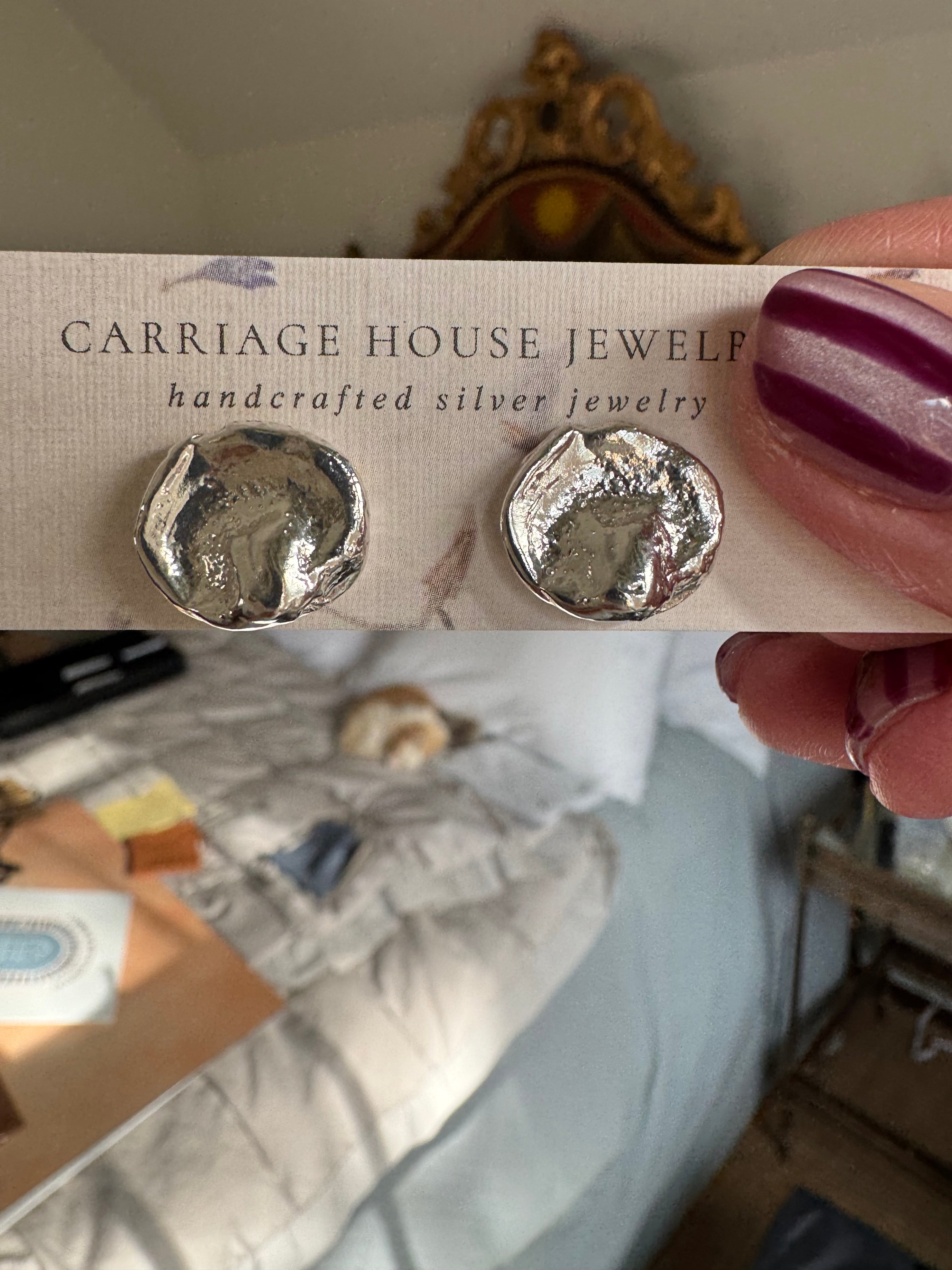 Silver earrings held on a Carriage House Jewelers card with a blurred background