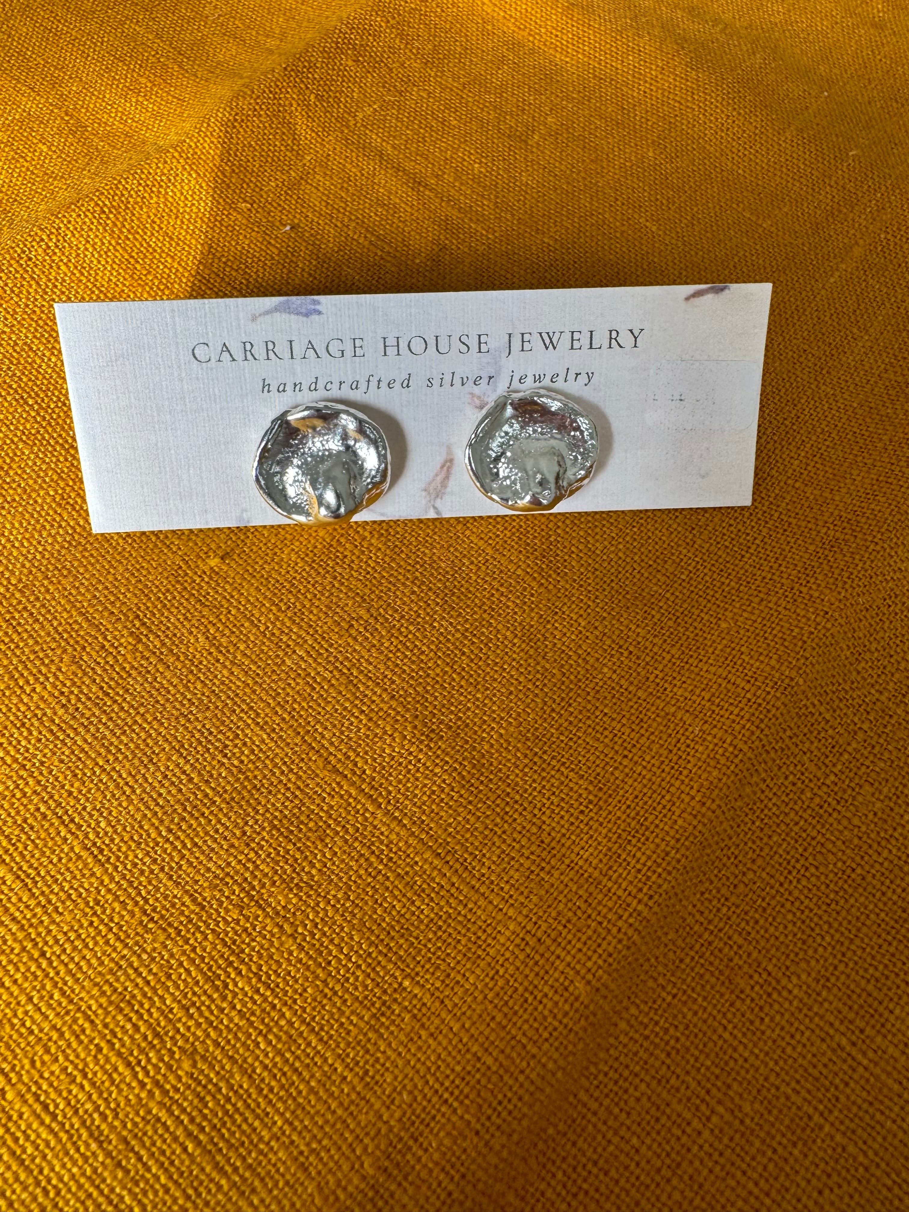 Pair of silver earrings on a 'Carrage House Jewelry' card against a yellow fabric background