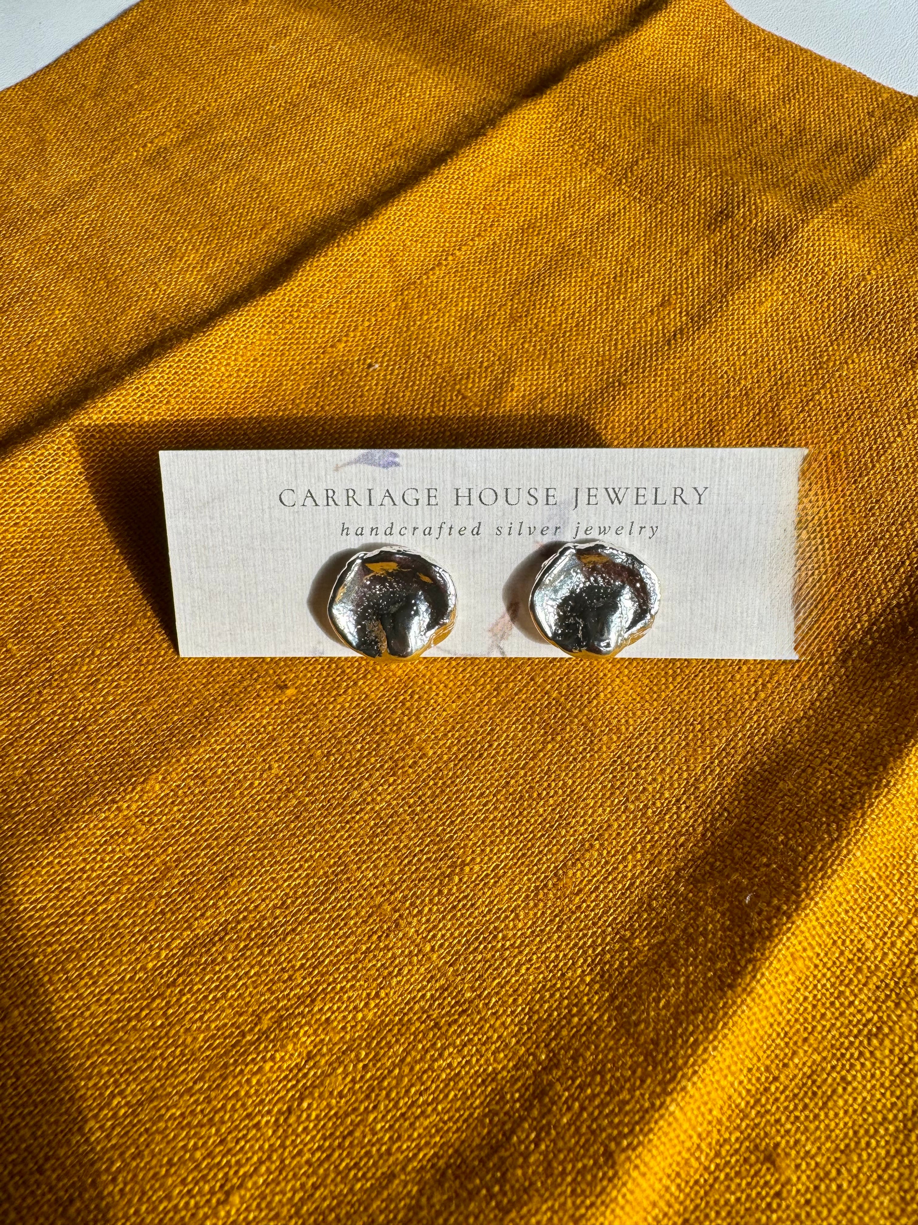 Silver earrings on a 'Carriage House Jewelry' card against a mustard yellow fabric background