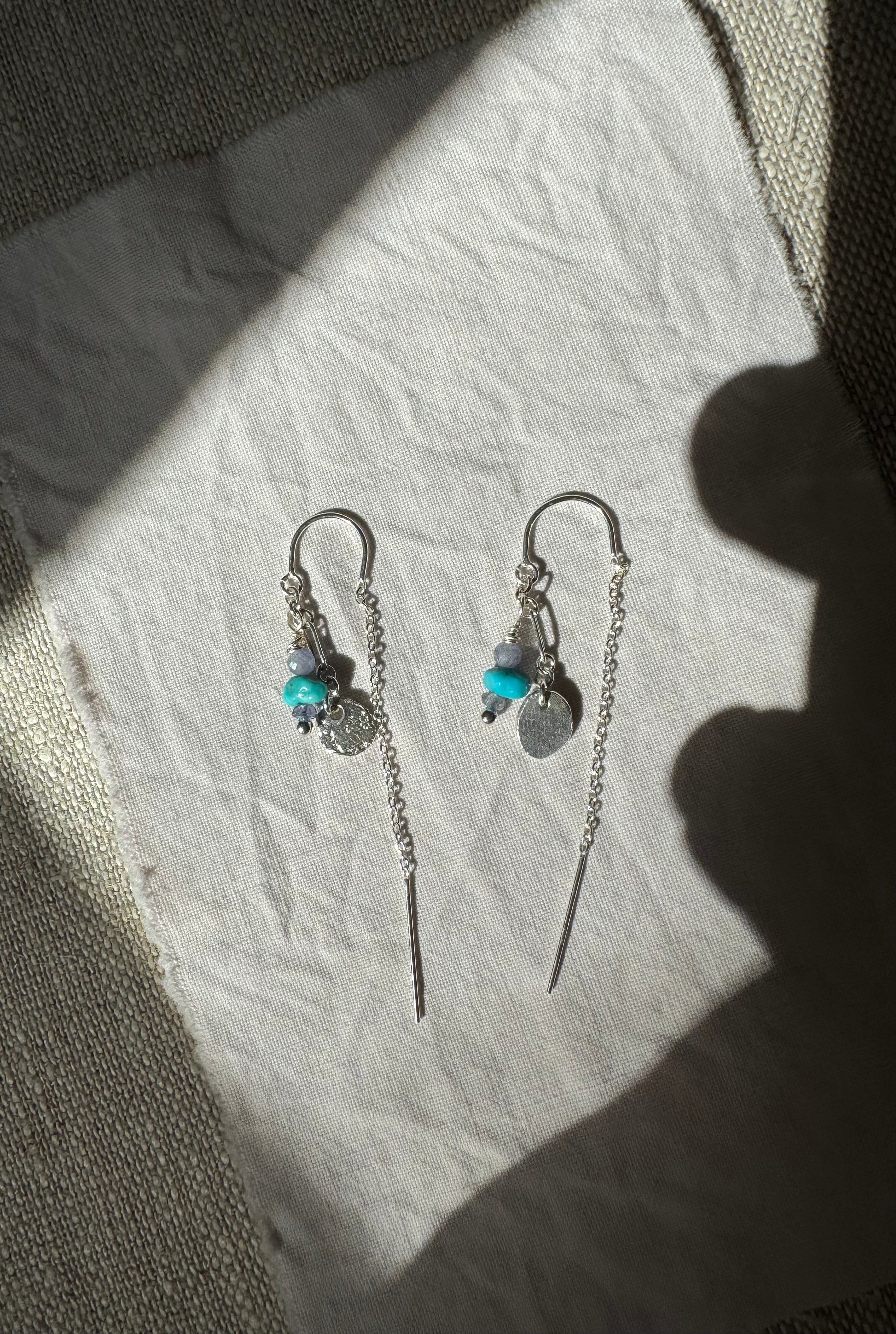 Pair of silver earrings with turquoise stones on a textured surface