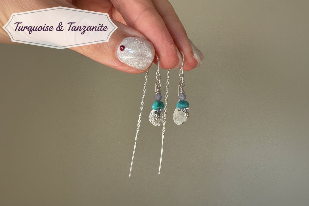 Hand holding a pair of silver and turquoise beaded earrings against a neutral background