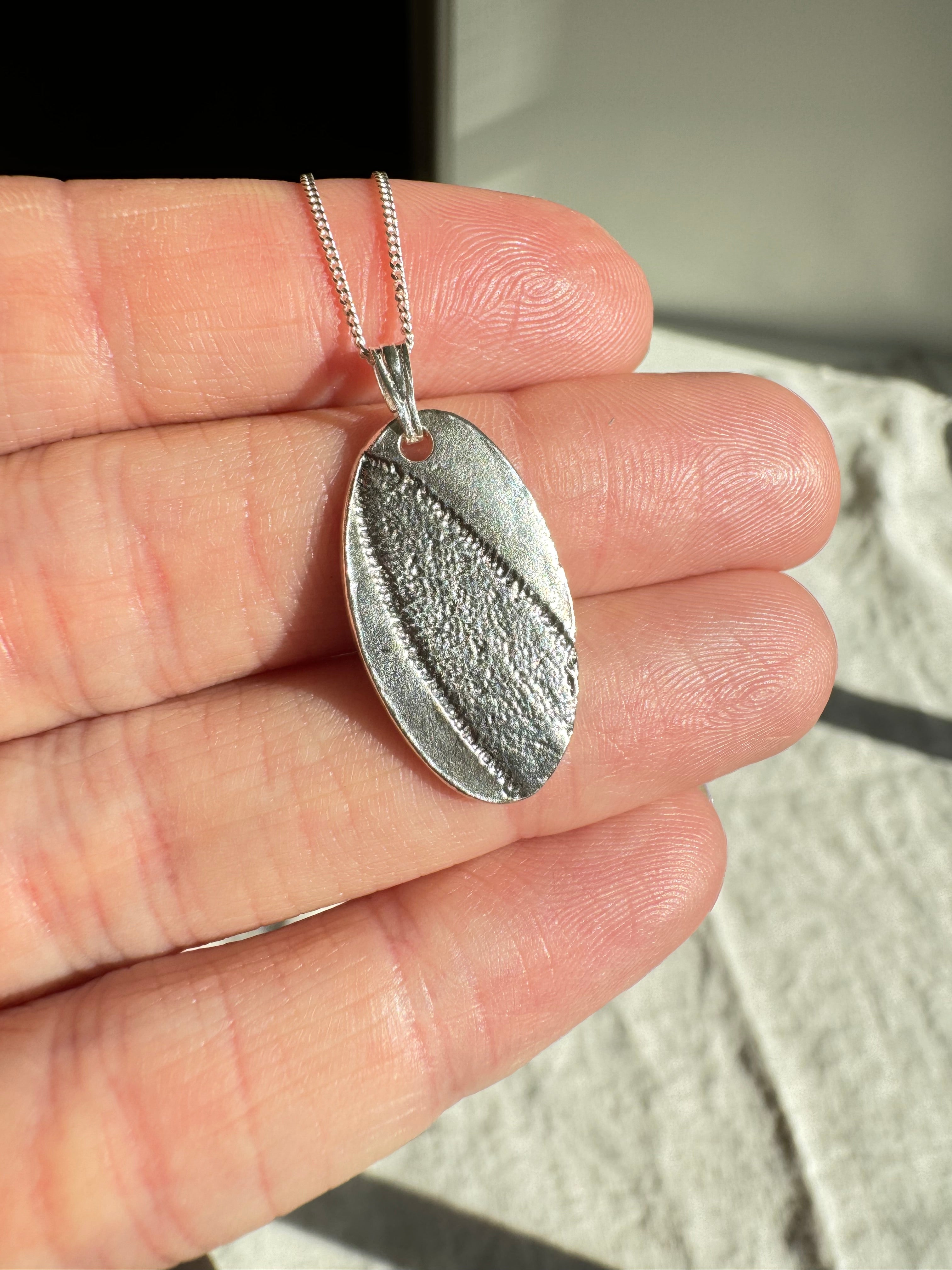 Hand pressed sage on fine silver with a sterling silver bail. Choose between a 16” or 18” sterling silver diamond cut curb chain.