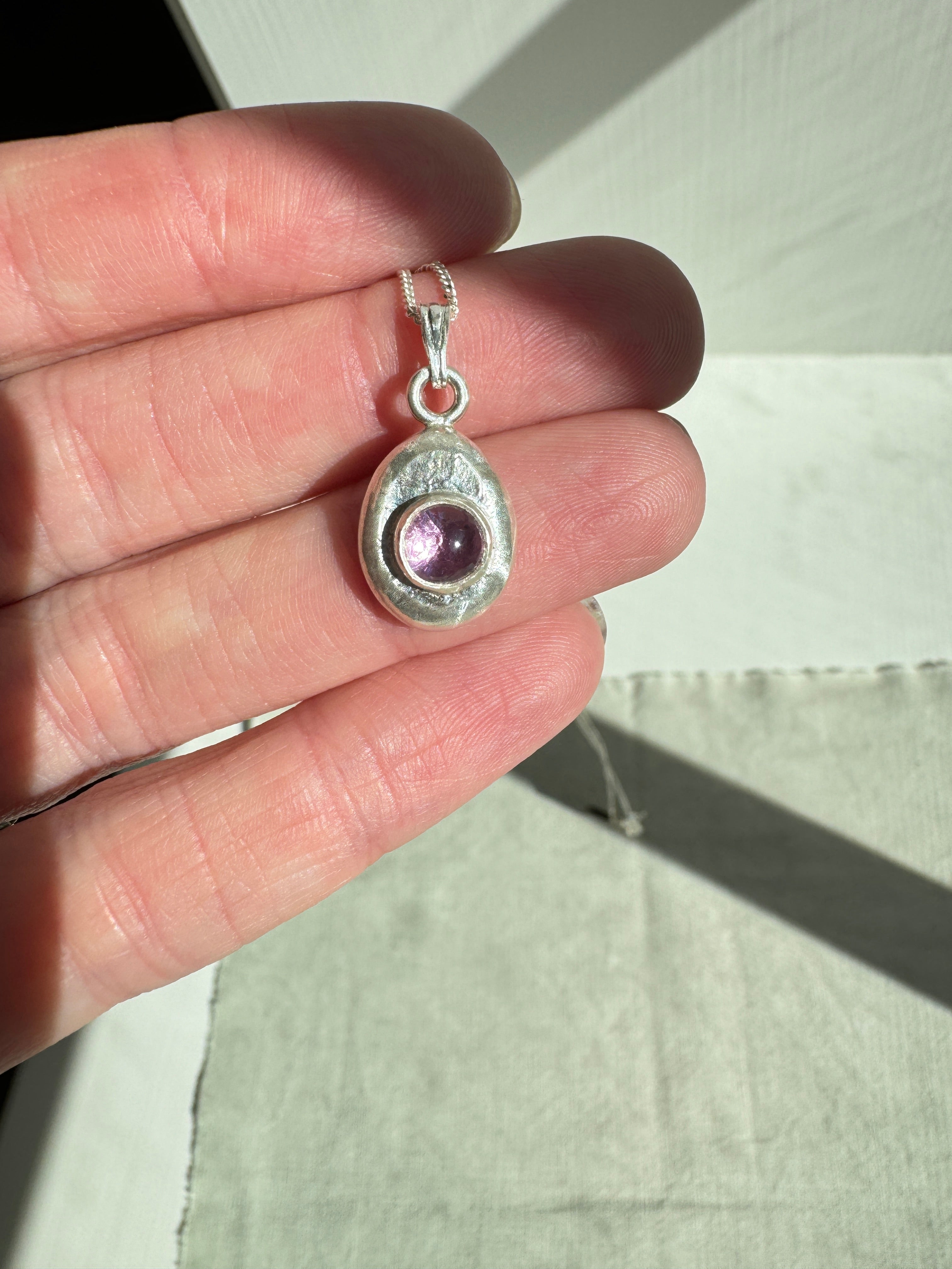 6mm Pink Sapphire (lab created) on a hand forged nugget of sterling silver. Choose between a 16” or 18” sterling silver diamond cut curb chain.