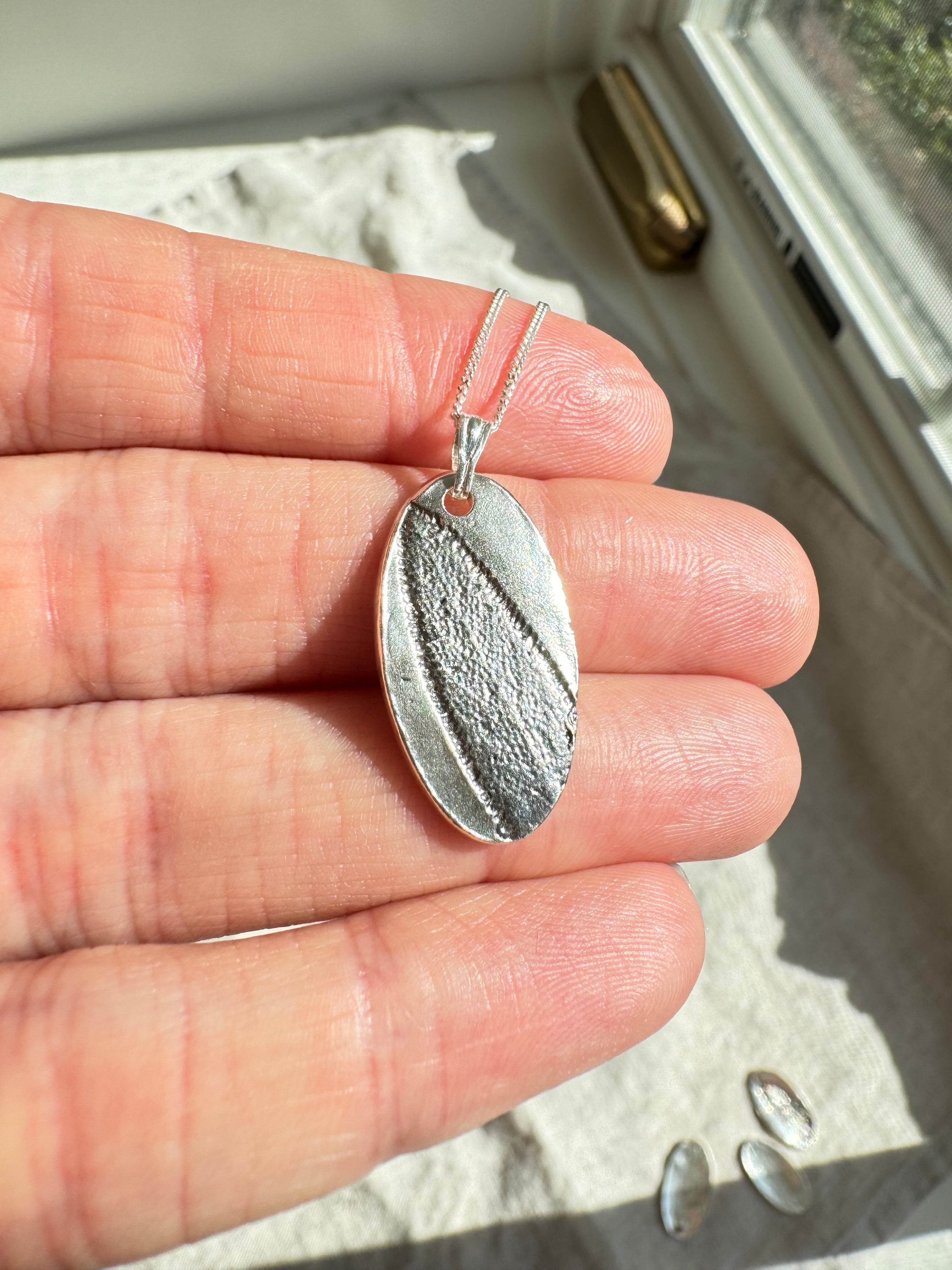 Hand pressed sage on fine silver with a sterling silver bail. Choose between a 16” or 18” sterling silver diamond cut curb chain.