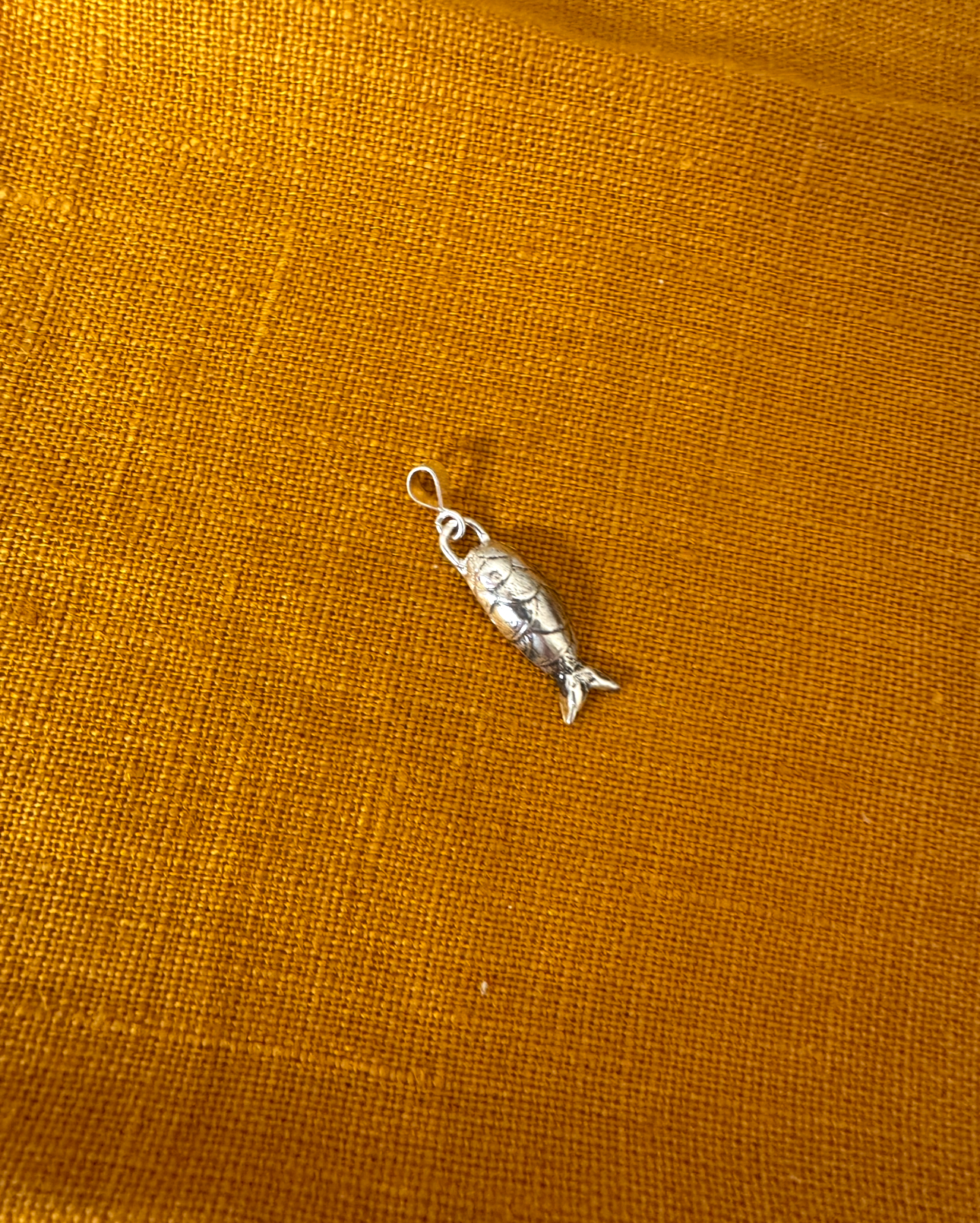 Silver fish charm on a mustard yellow fabric background